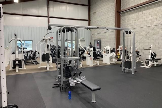 Indoor gym with cable machines, benches, and weight equipment on a black floor.