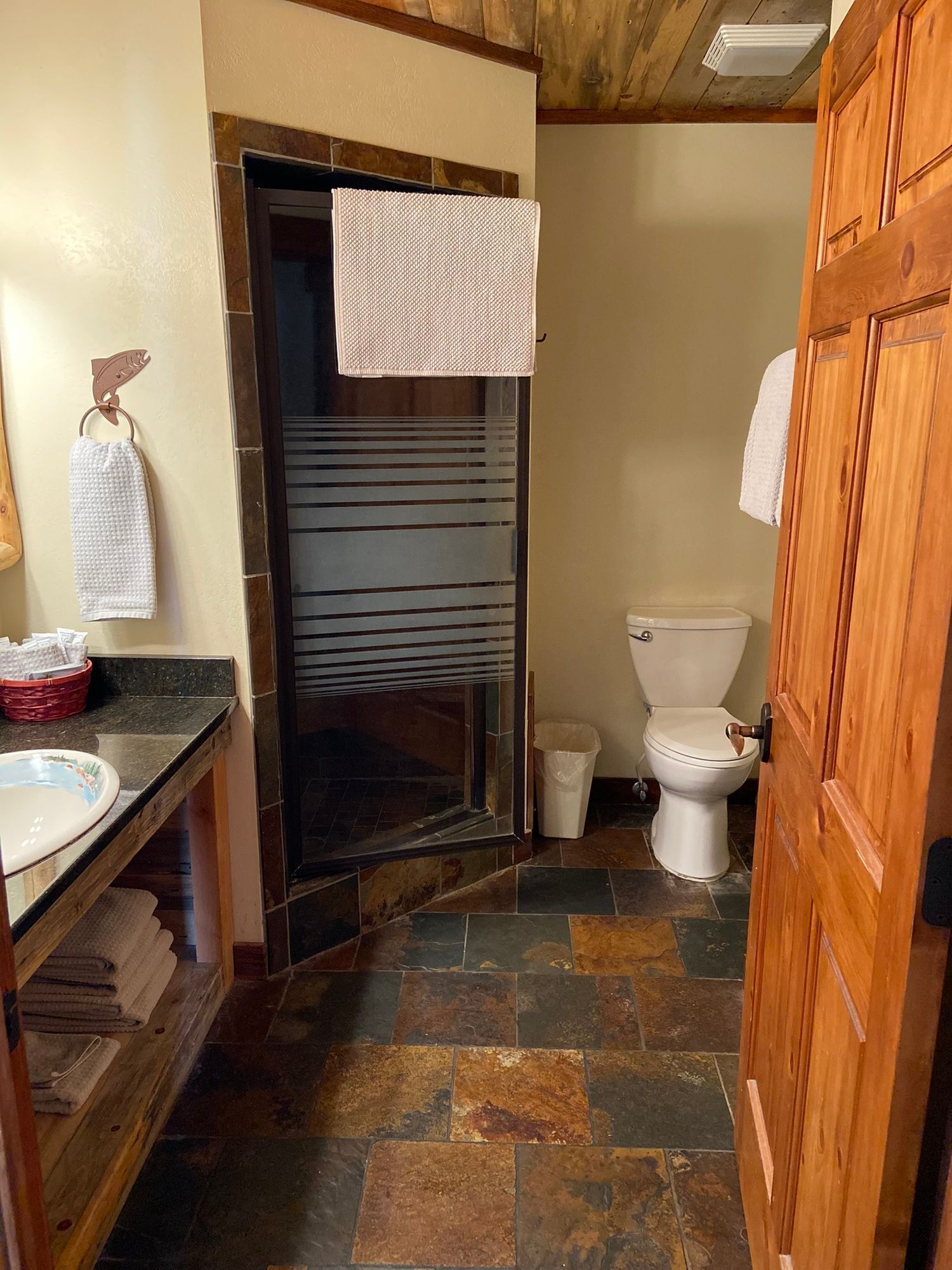 Small bathroom with sink, shower stall, toilet, and wood-paneled door.