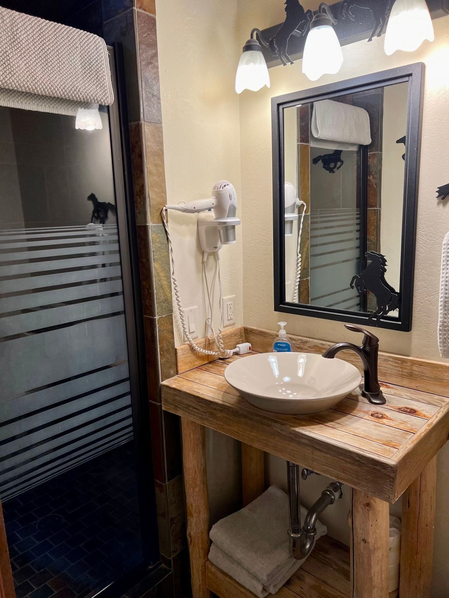 Rustic bathroom vanity with vessel sink, black mirror, wooden countertop, and frosted glass shower door