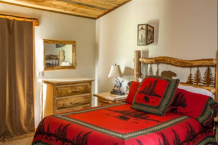 Cozy bedroom with a red bedspread, wooden dresser, mirror, lamp, and framed wall art
