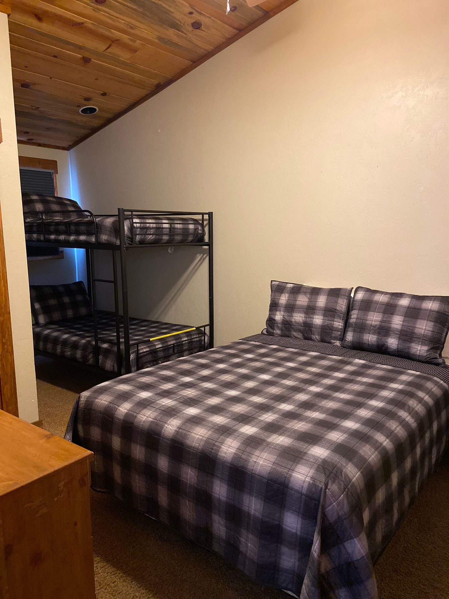 Small bedroom with plaid bedspread, bunk bed, slanted wood ceiling, and plain beige wall
