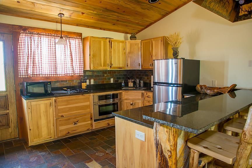 Rustic kitchen with wood cabinets, black countertops, stainless fridge, and a wood ceiling