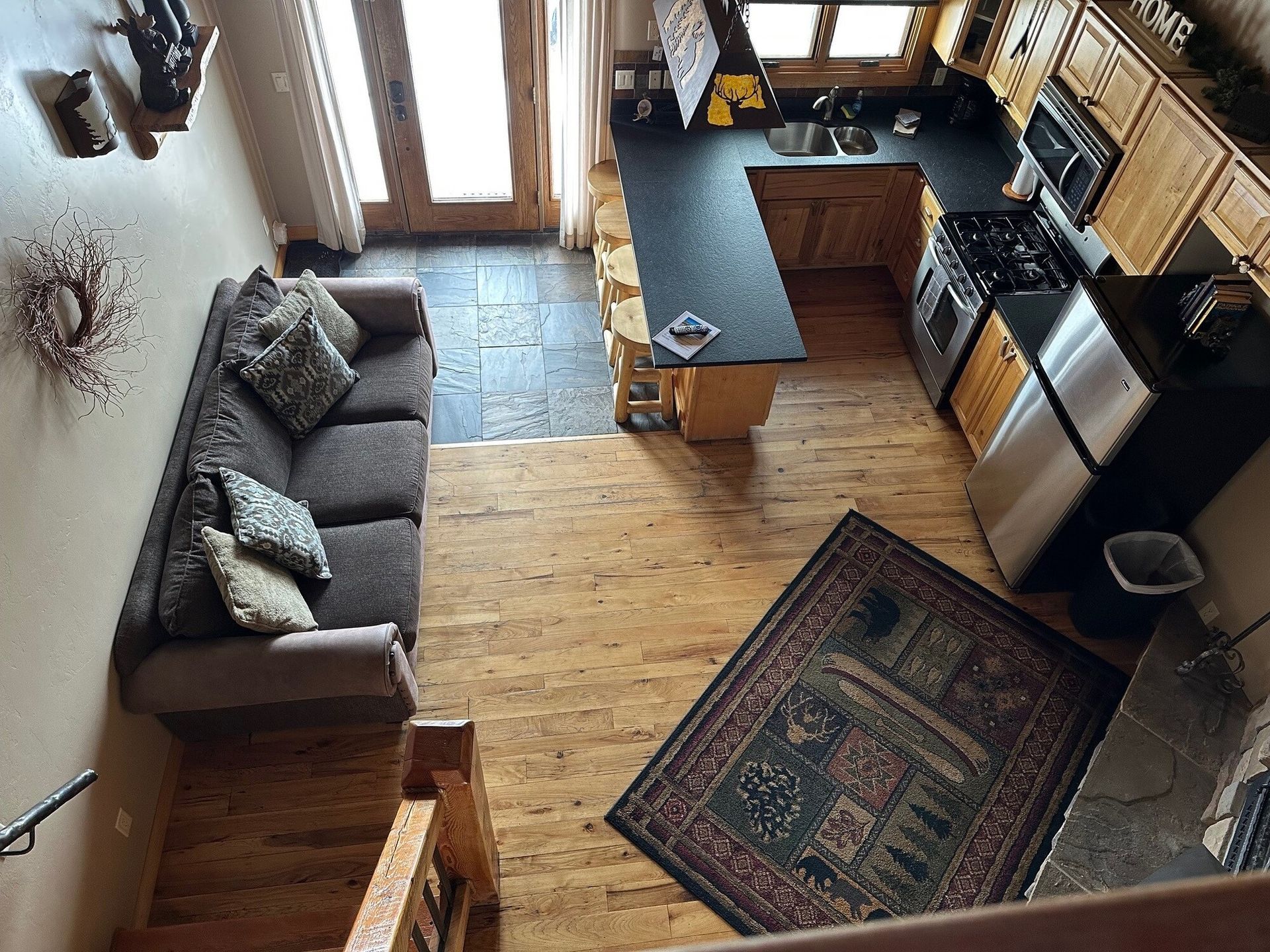 Compact kitchen-living room with gray sofa, wooden floor, dark rug, and black countertops by a window.