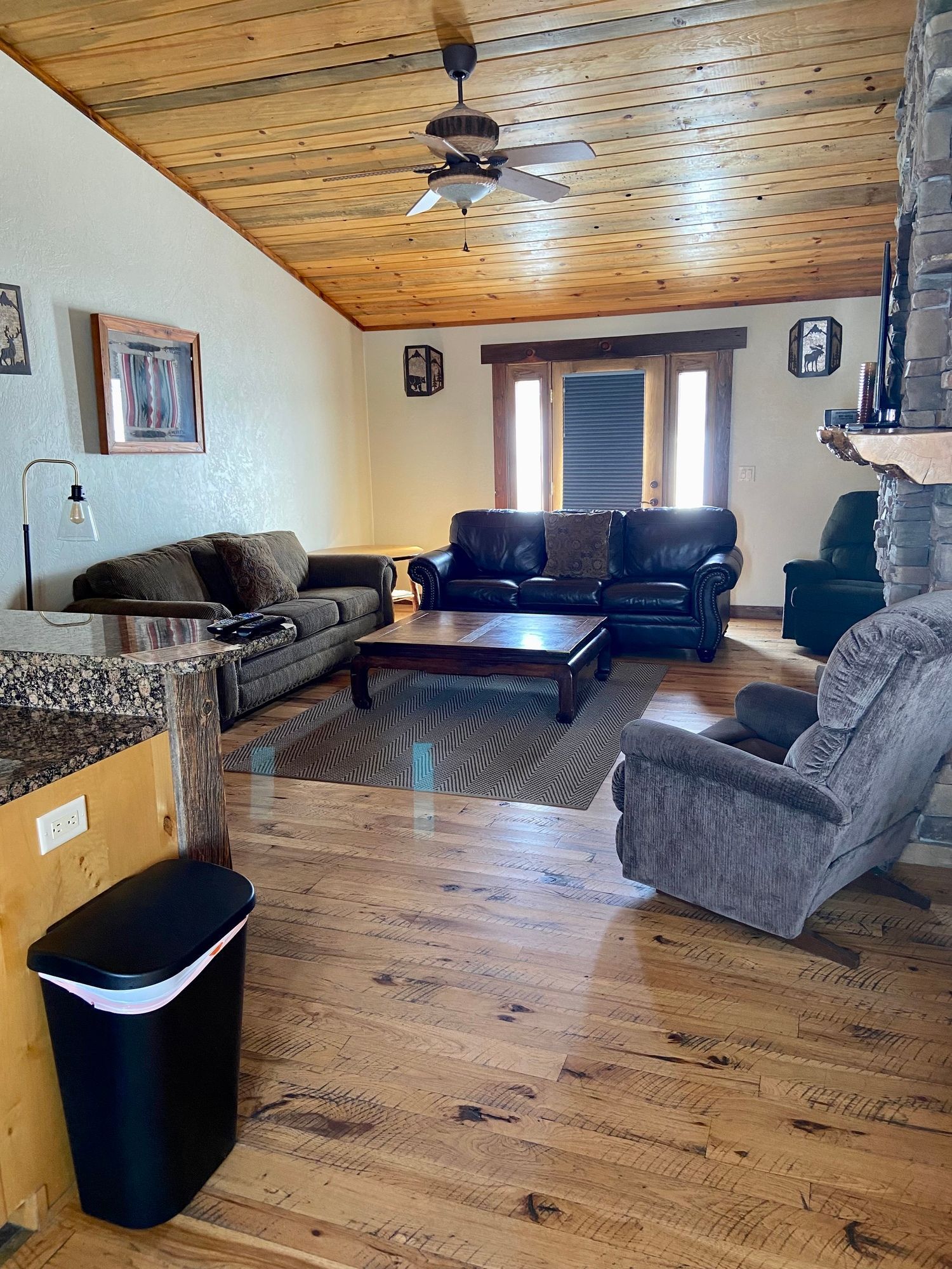Cozy living room with wood-paneled ceiling, leather sofas, patterned rug, and a coffee table near a window.