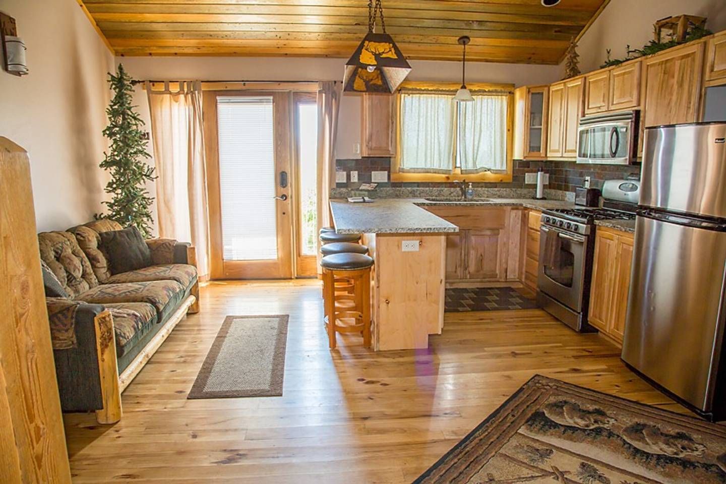 Cozy wood-paneled kitchen and living area with stainless fridge, island, couch, and glass doors to outside