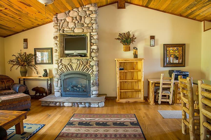 Cozy living room with stone fireplace, wooden ceiling, rustic furniture, and patterned rug