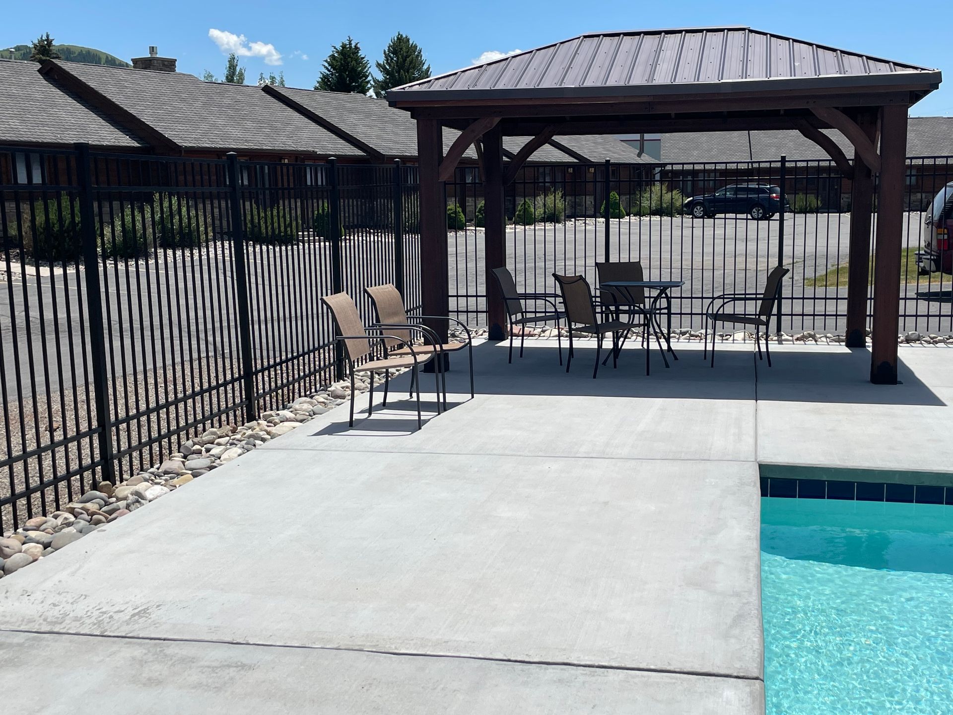 Poolside patio with gazebo, chairs, black fence, and turquoise pool water