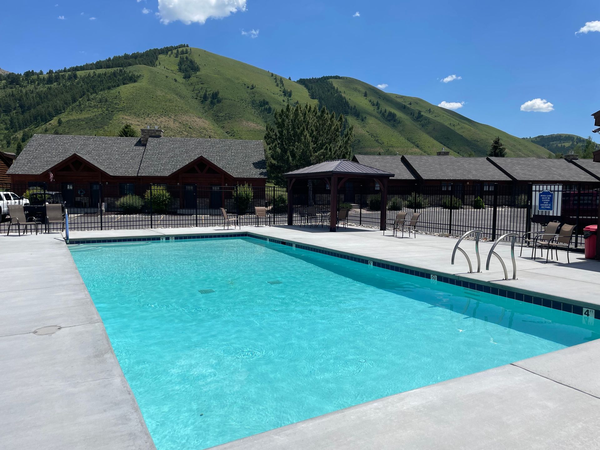 Outdoor pool with turquoise water beside mountain lodges under a clear blue sky