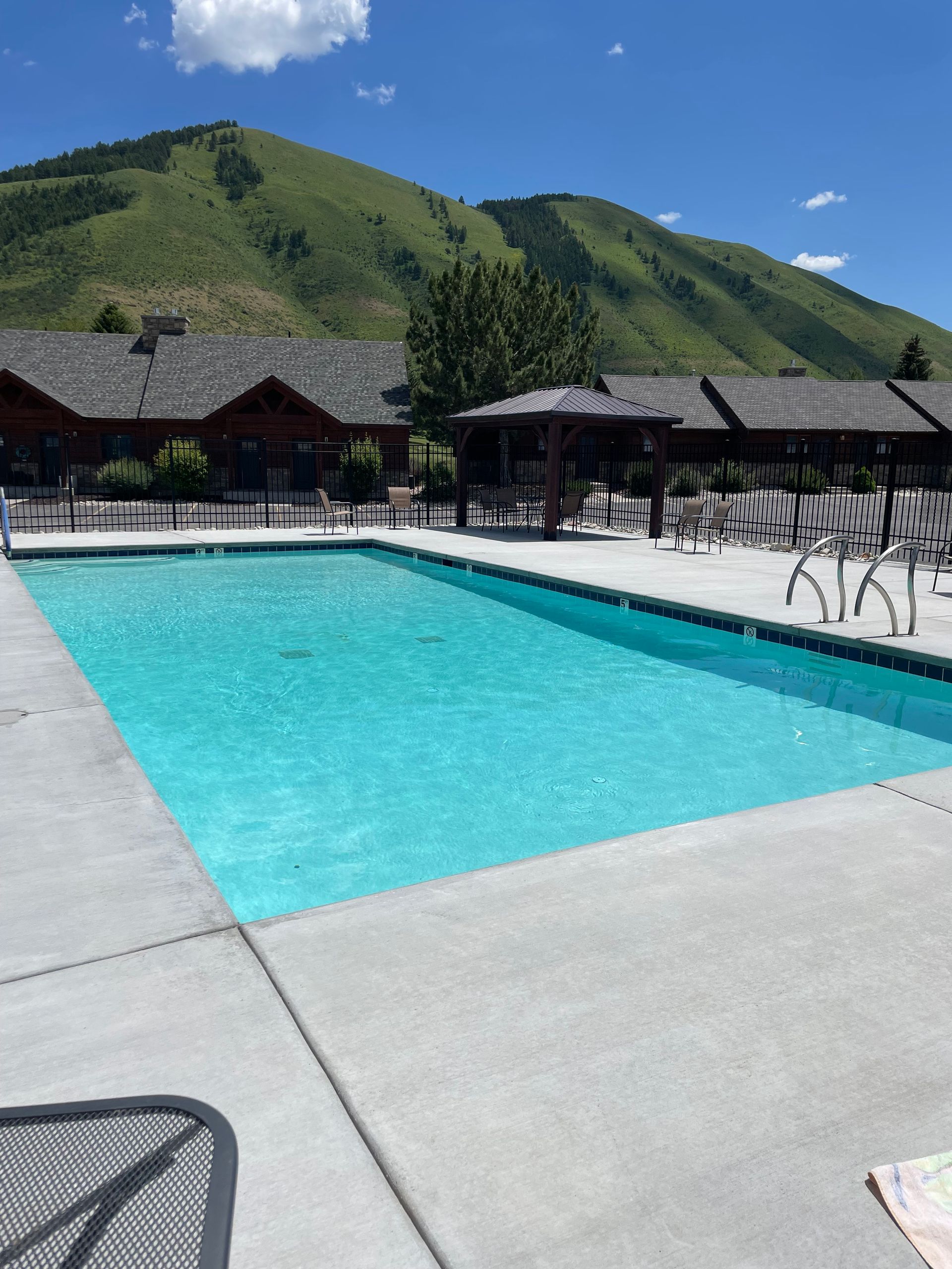 Outdoor pool with turquoise water, lounge chairs, and green hills under a blue sky