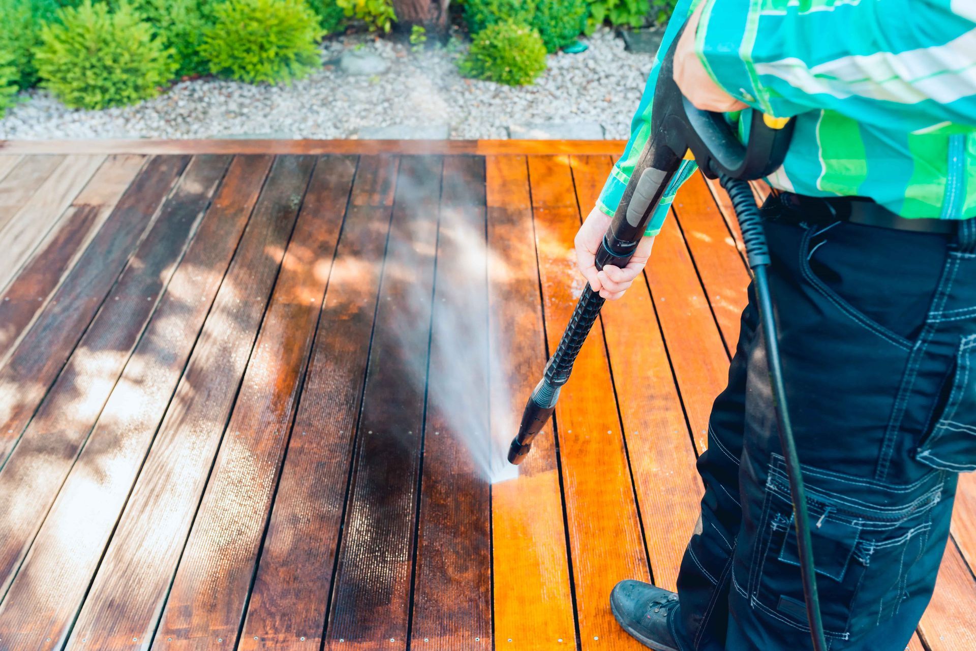 Man power washing a wooden deck, revealing clean wood.