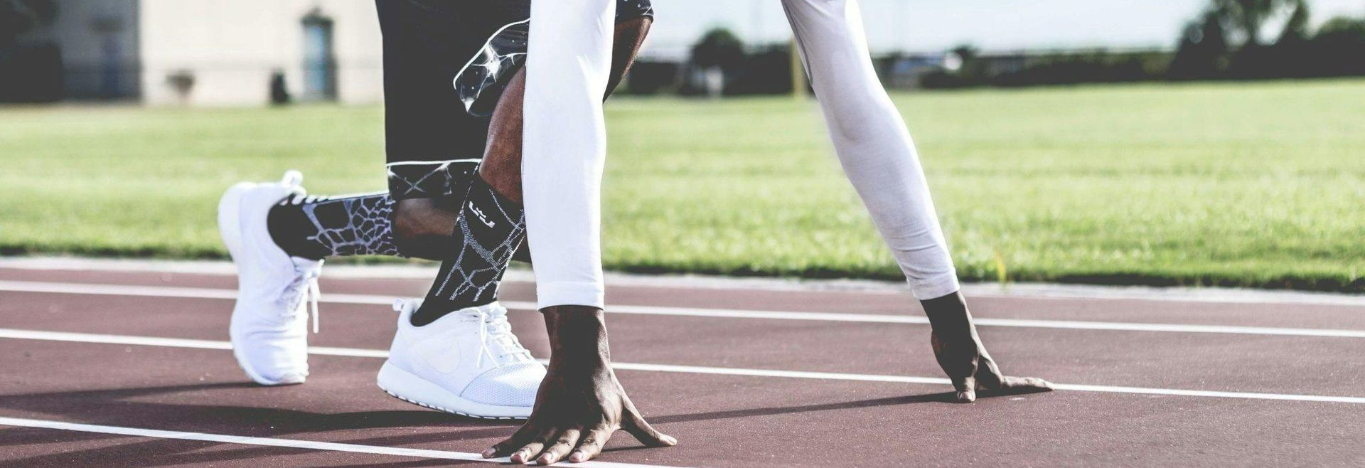 Athlete in starting position on a track, focused, white long sleeve, black shorts, white shoes.