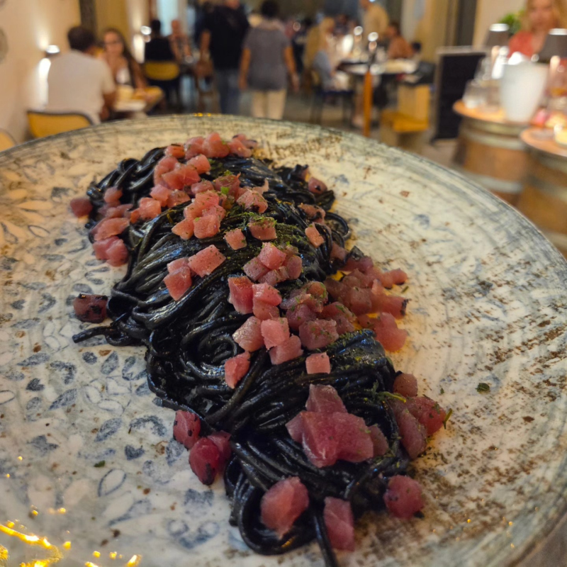 Pasta nera con salumi a cubetti su un piatto maculato in un ristorante