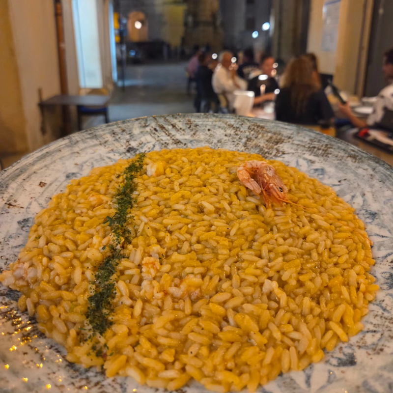 Un abbondante piatto di risotto giallo con guarnizione verde e gamberi in un ristorante dalle luci soffuse.