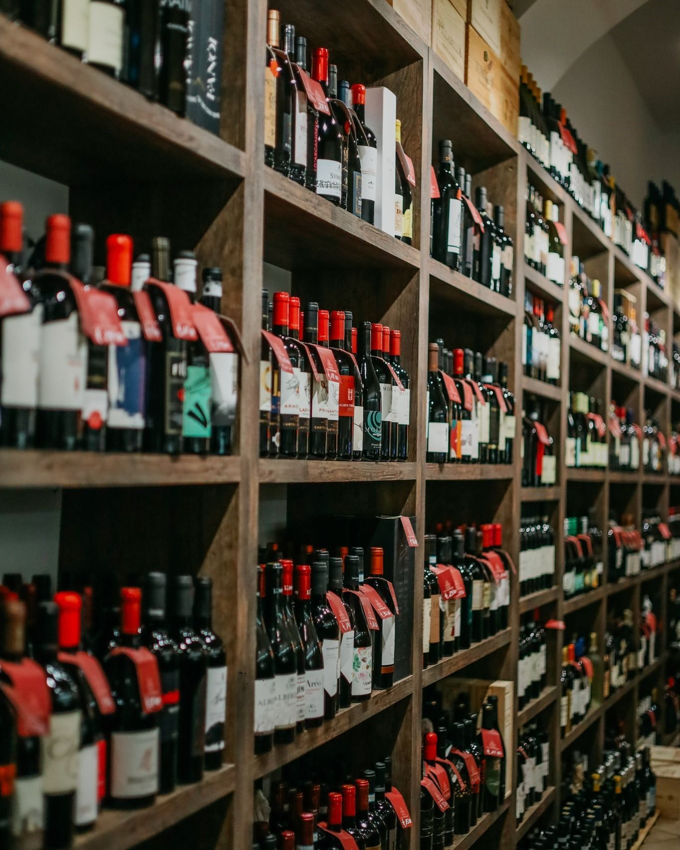 File di bottiglie di vino con tappo rosso su scaffali di legno in un'enoteca o in una cantina.