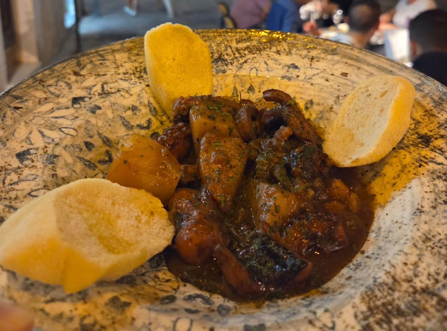 Primo piano di un piatto di carne con salsa in una ciotola maculata con fette di pane a lato.