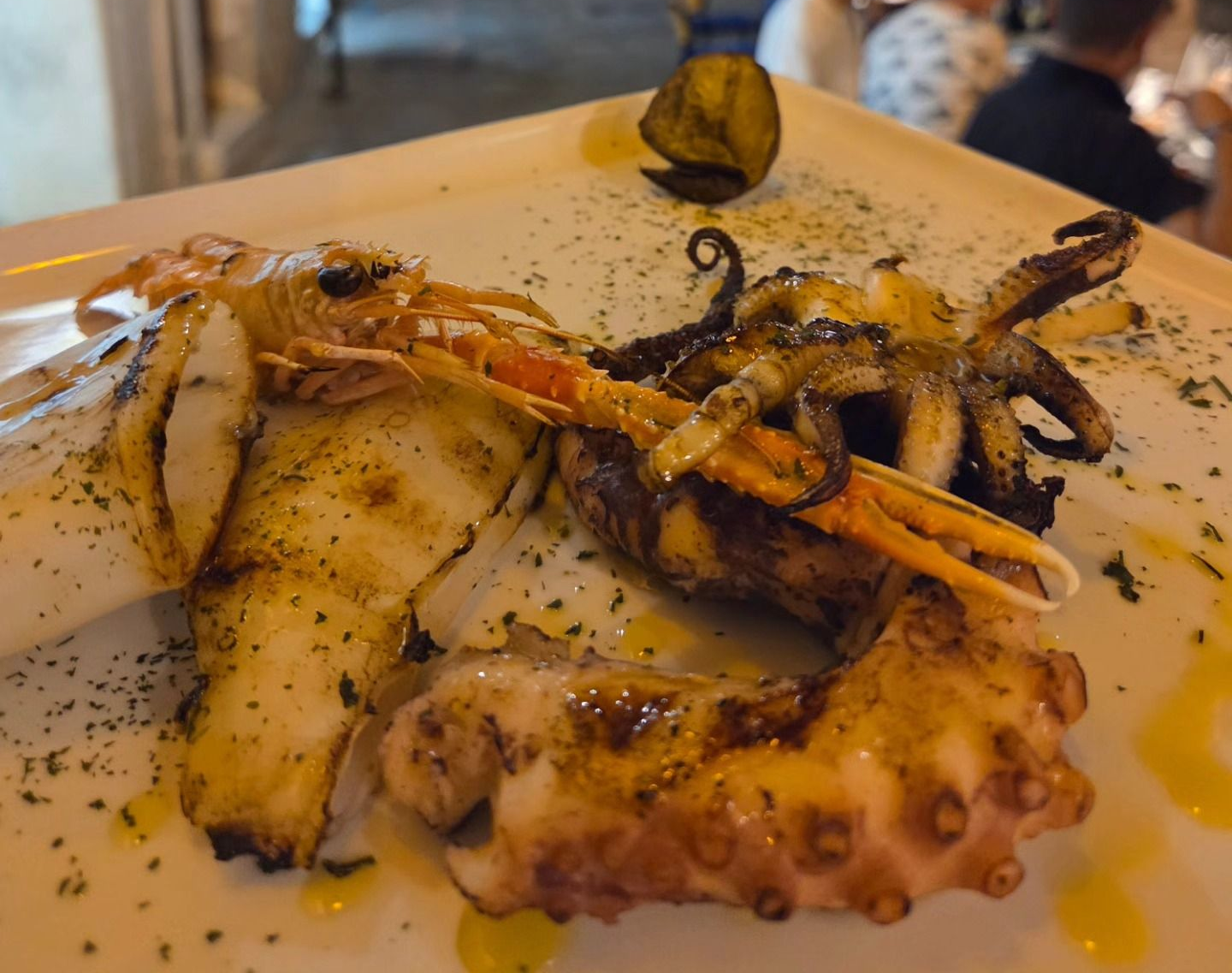 Piatto di frutti di mare grigliati con polpo e pesce su un piatto bianco, condito con un filo d'olio e erbe aromatiche.