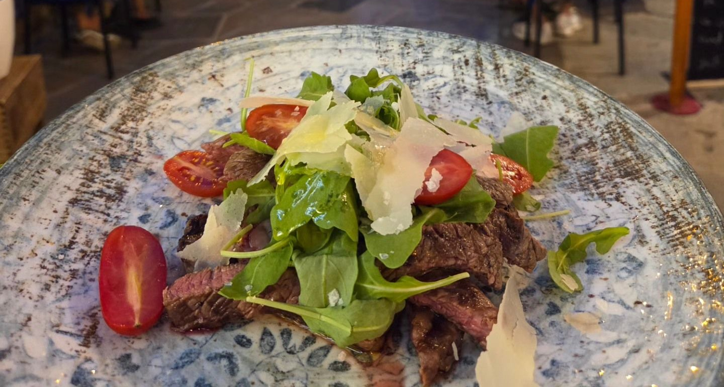 Insalata di bistecca aperta con rucola, formaggio grattugiato e pomodorini su un piatto blu