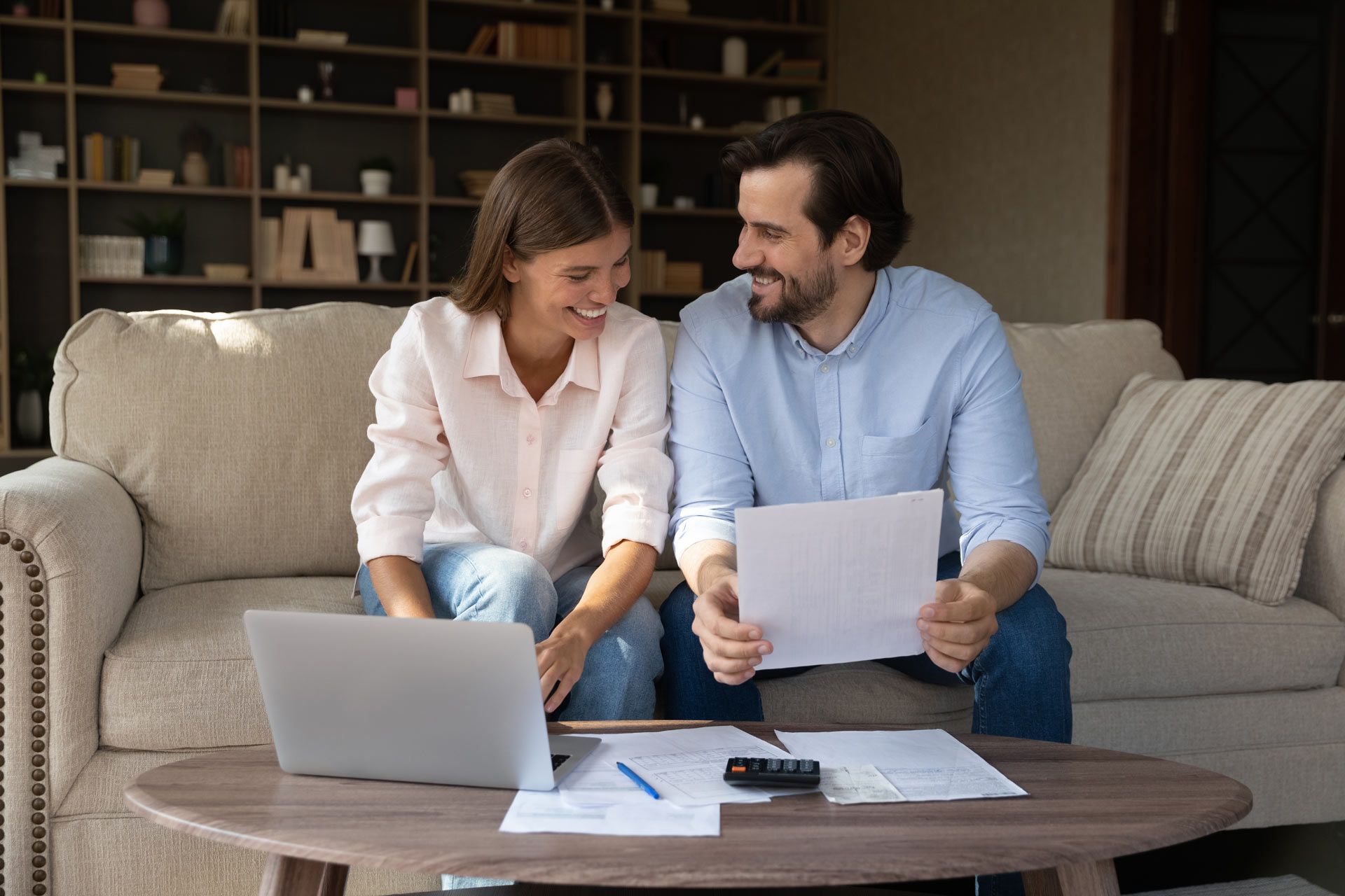 A man and a woman are sitting on a couch looking at papers and a laptop