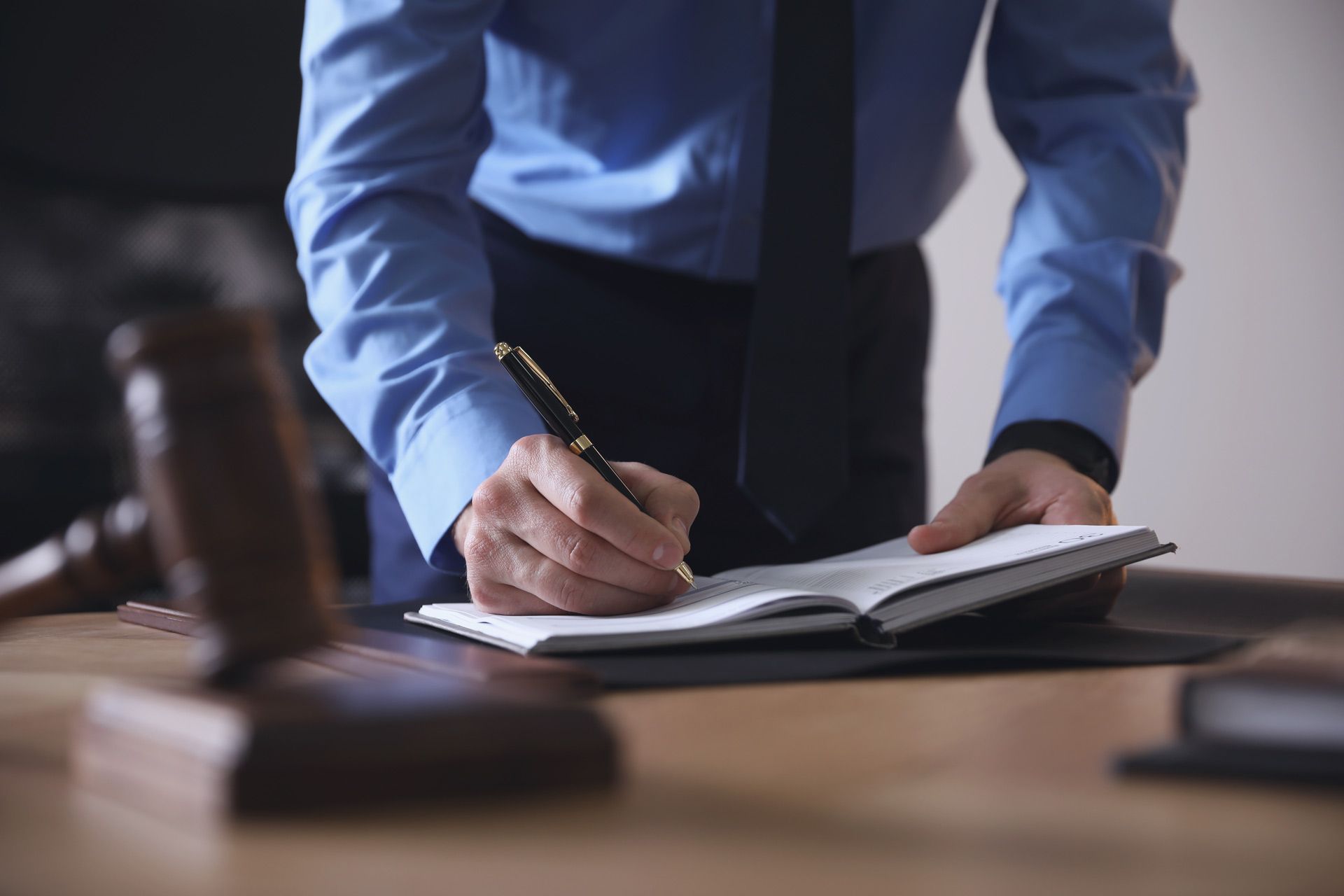 A man in a blue shirt and tie is writing in a notebook