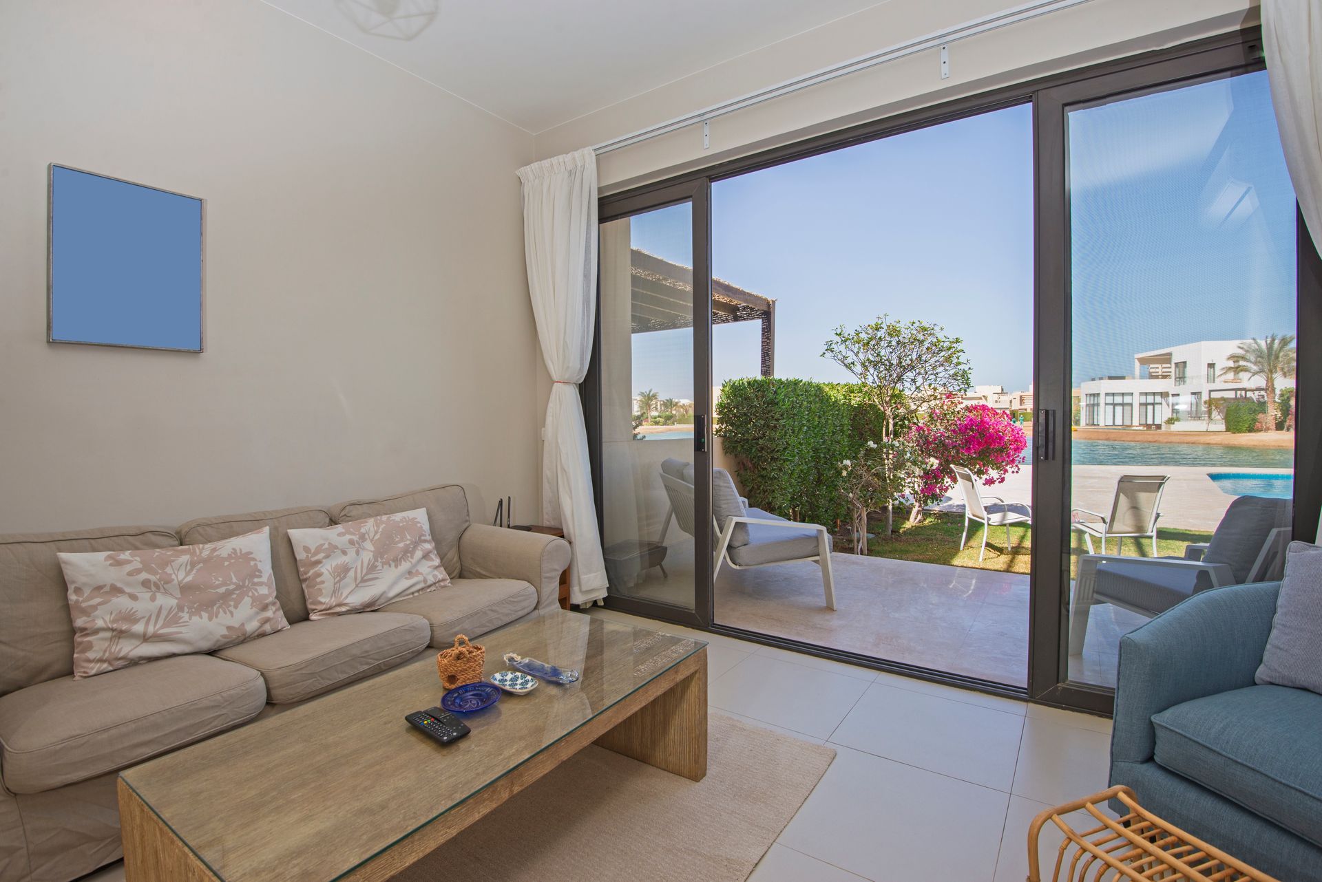 Modern living room with beige sofa, coffee table, blue chair, and open sliding doors to a sunny patio.