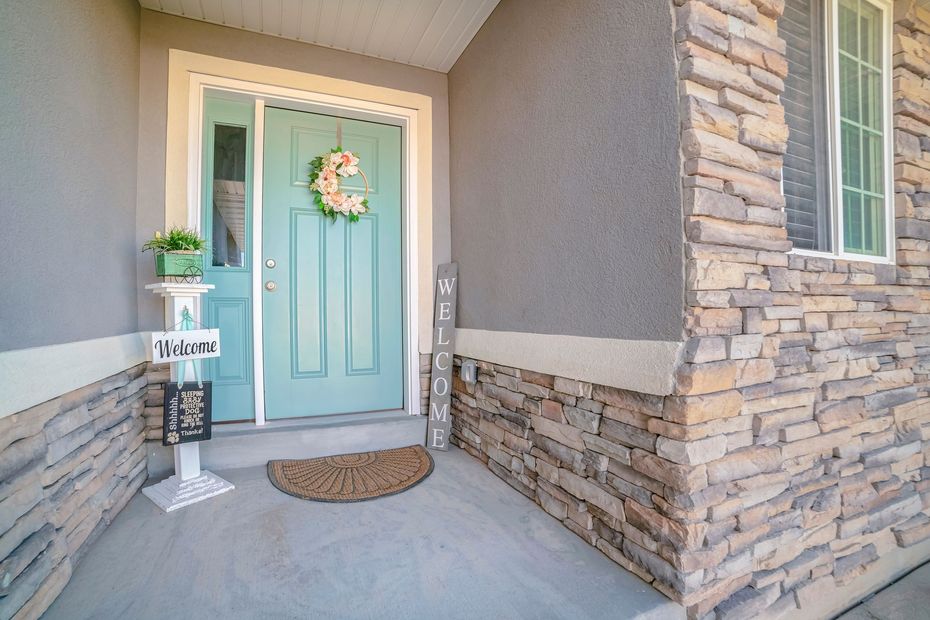 Front porch with aqua front door, stone siding, welcome wreath, and potted plants