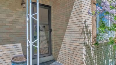 Brick apartment entrance with a glass door, white metal post, and window beside a small potted plant.