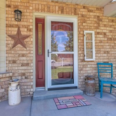 Brick house front porch with red door, star decor, blue chair, and doormat.