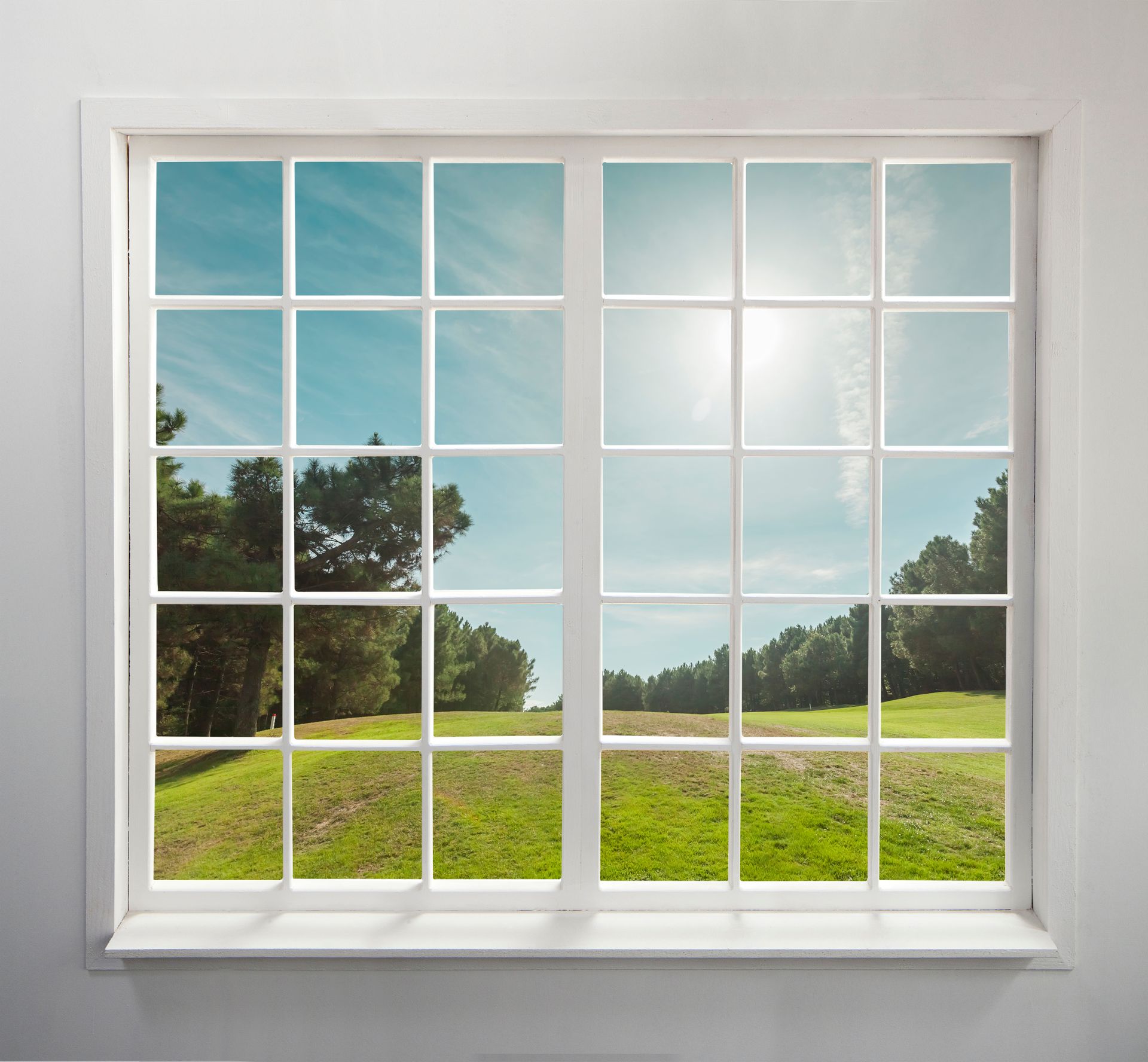 White-framed window with grid panes overlooking a sunny green field and blue sky