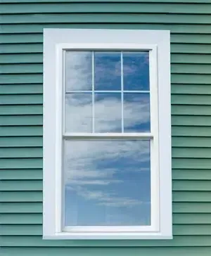White-framed window reflecting blue sky and clouds on green siding