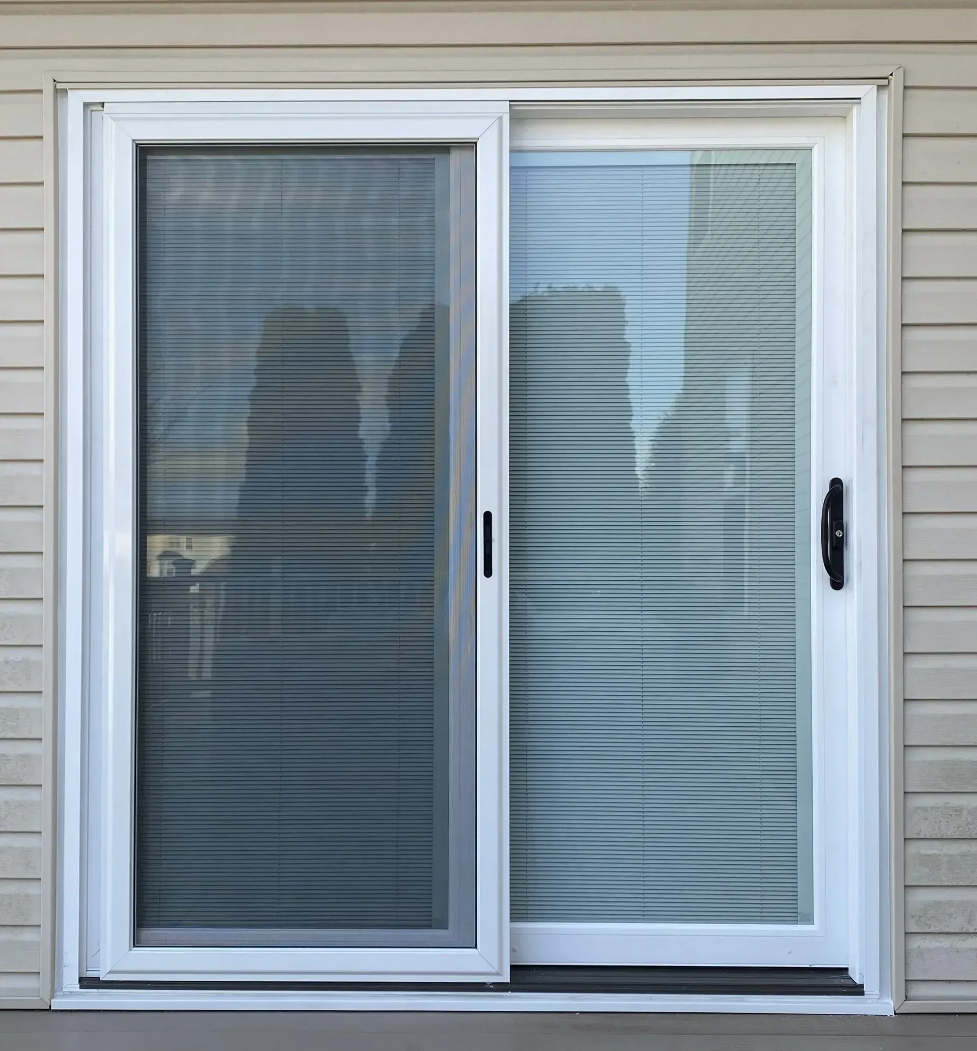White sliding glass patio door on beige siding with closed blinds behind the panes