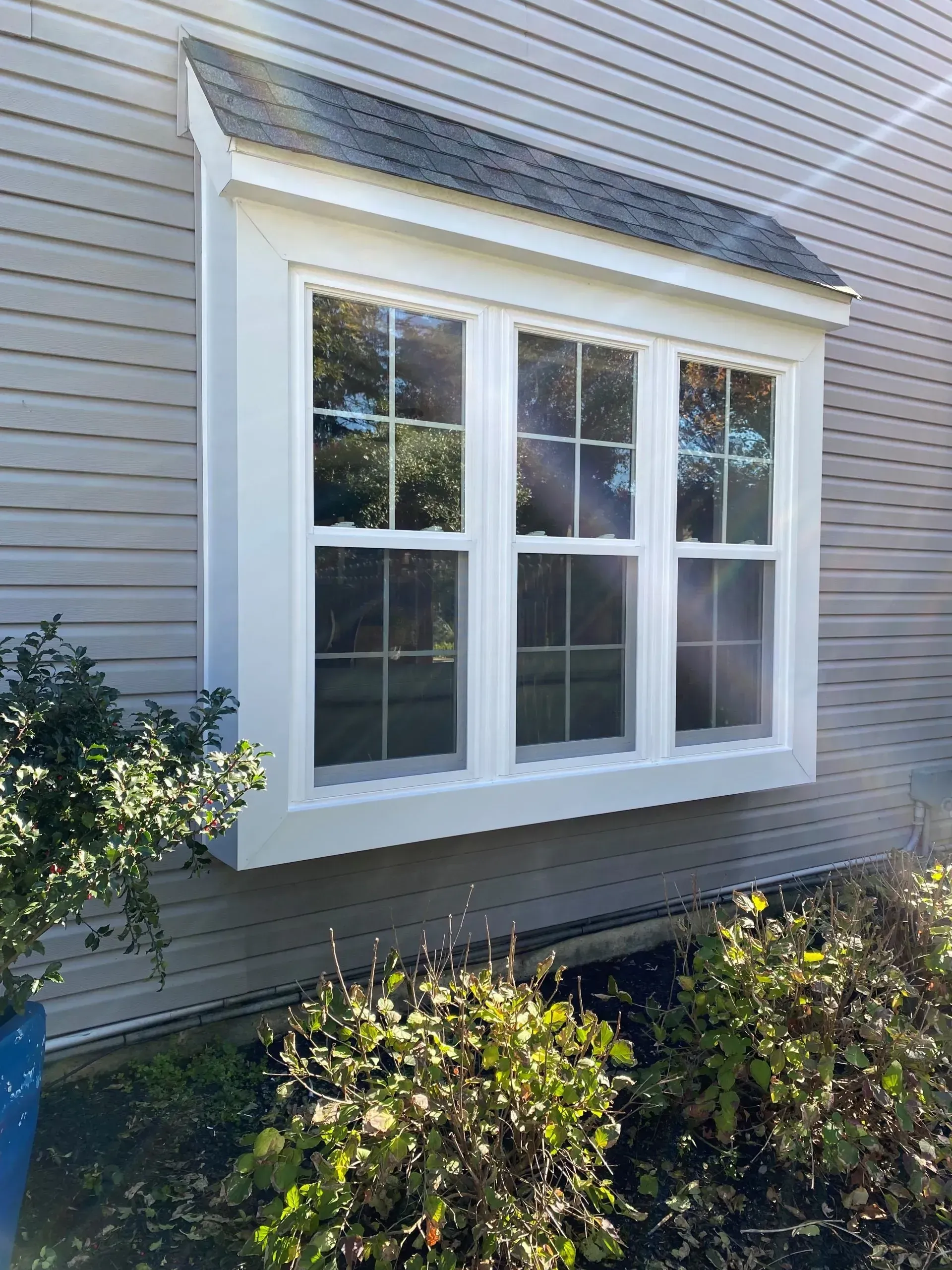 White-trimmed bay window on a gray house exterior with bushes below.