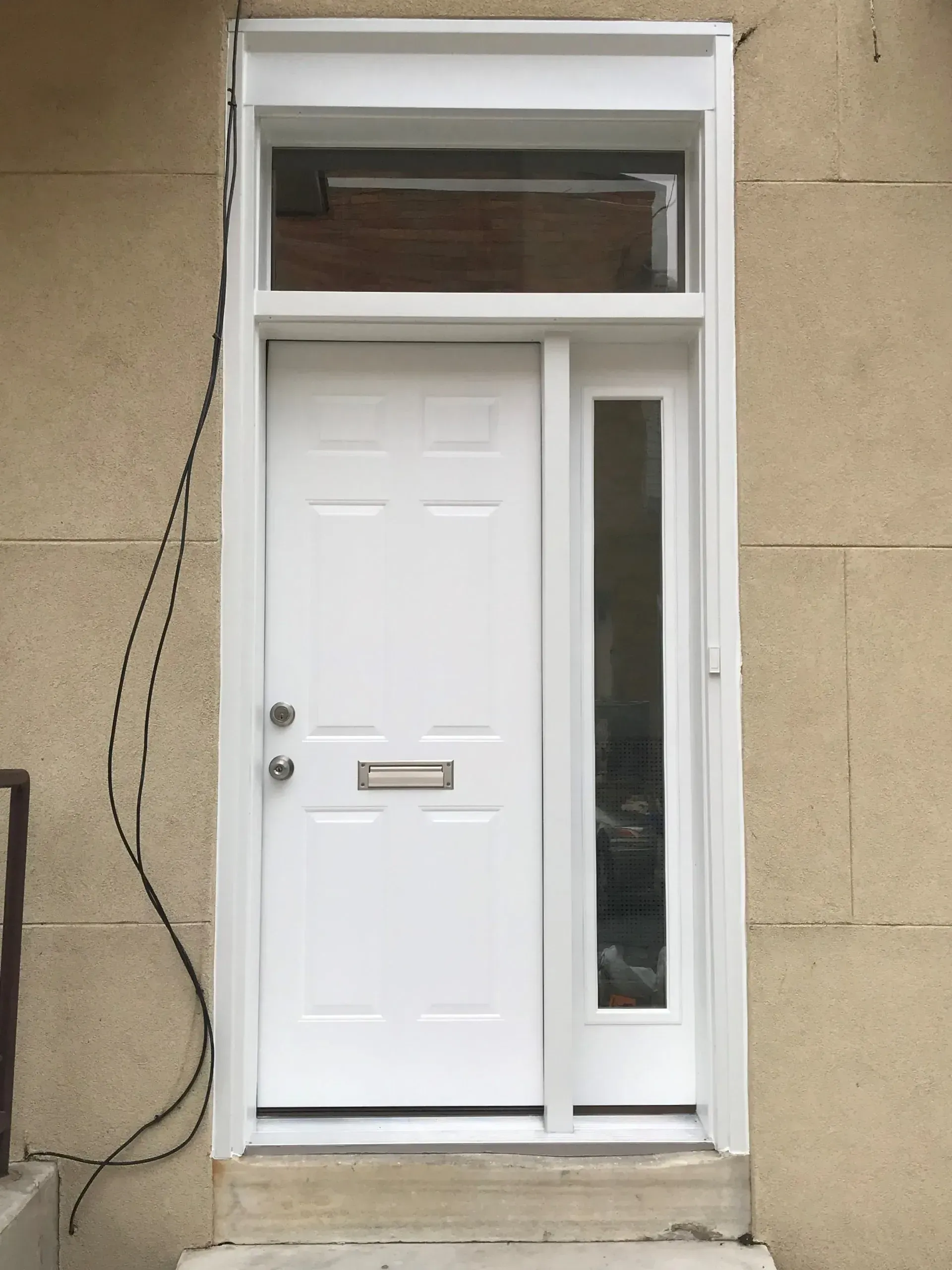 White front door with narrow side window and transom set in a beige exterior wall.