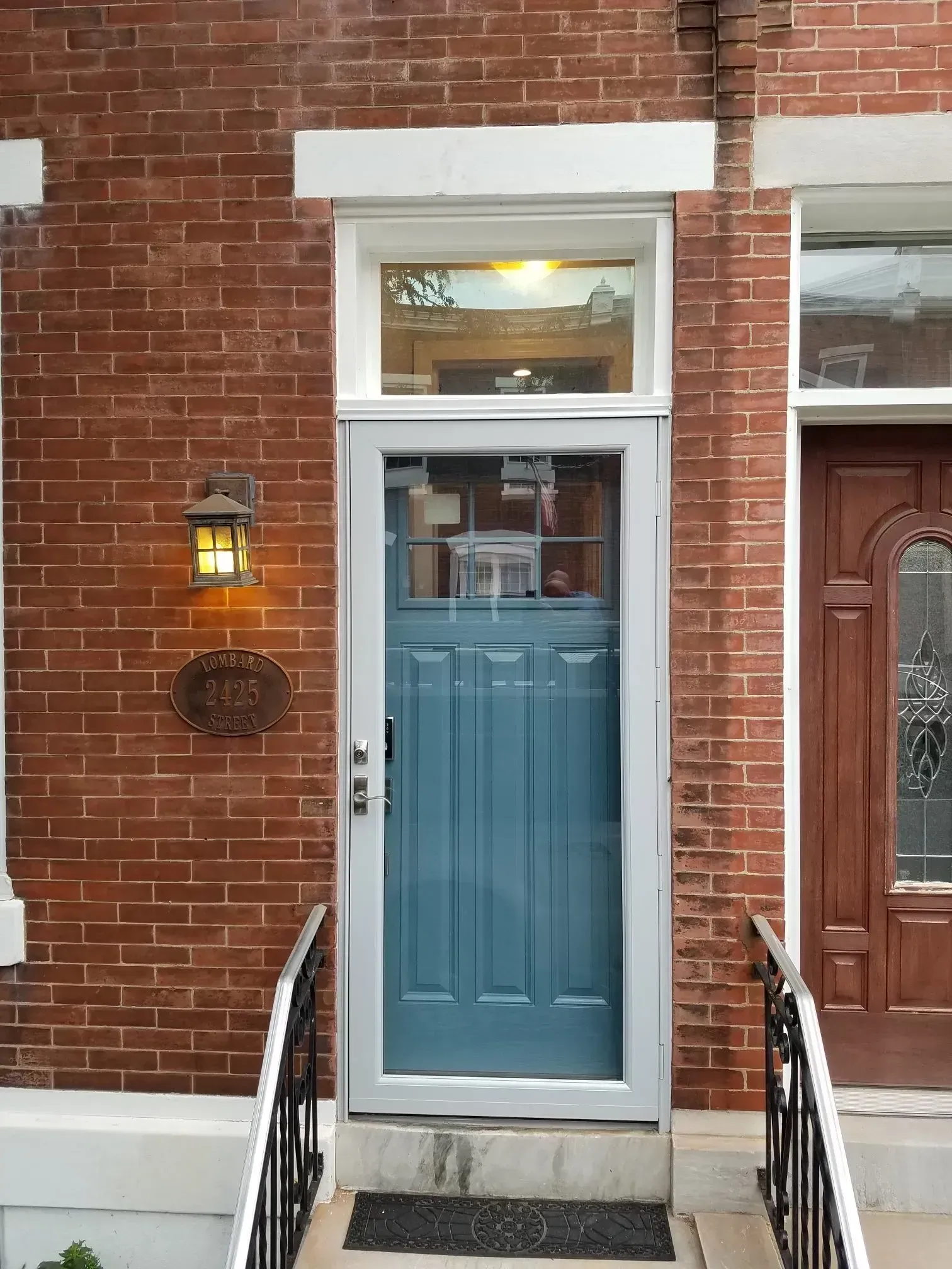 Blue front door on a brick townhouse with white trim and black railings