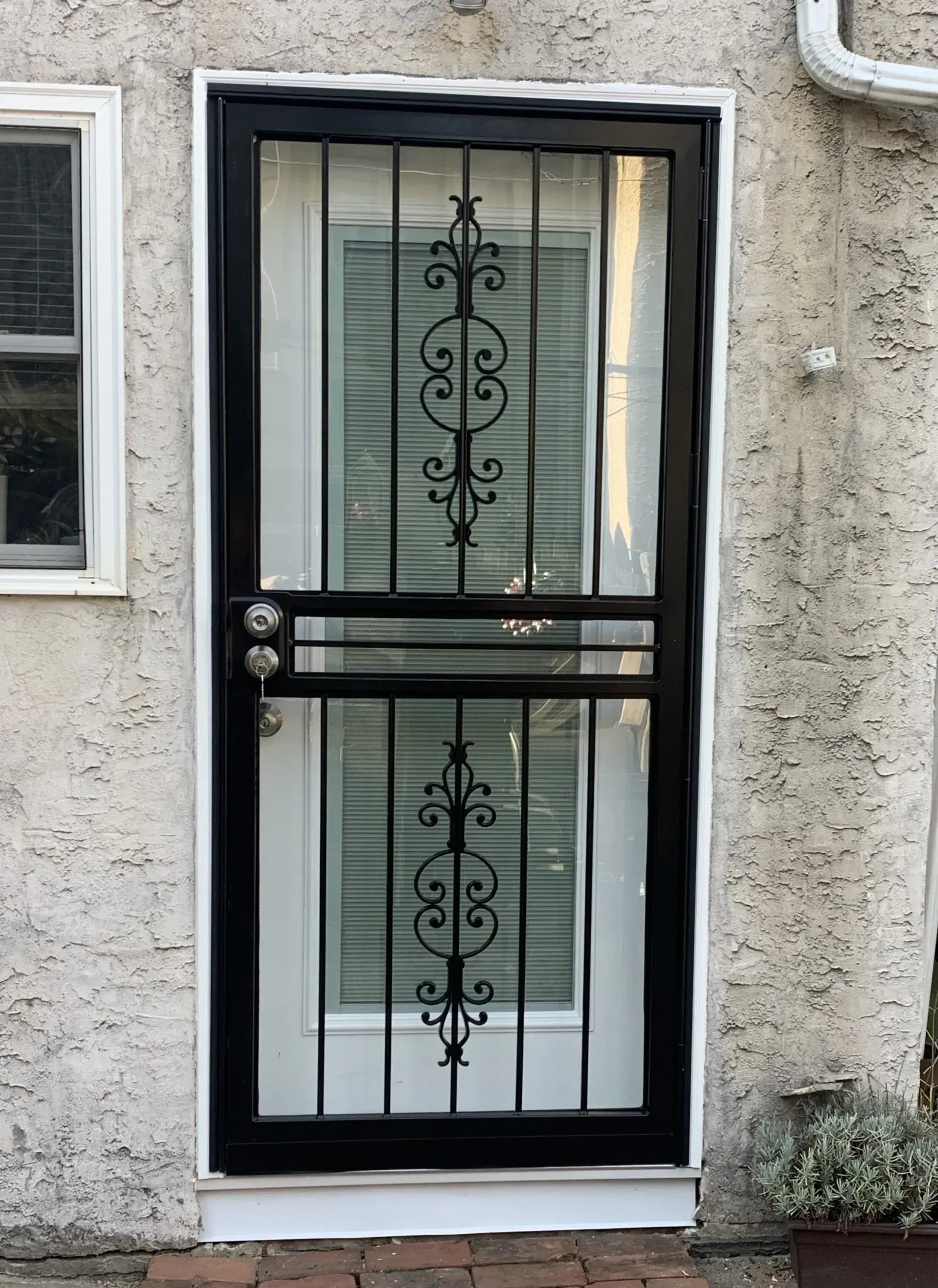 Black front door with decorative glass and metal grille on a stucco exterior wall.
