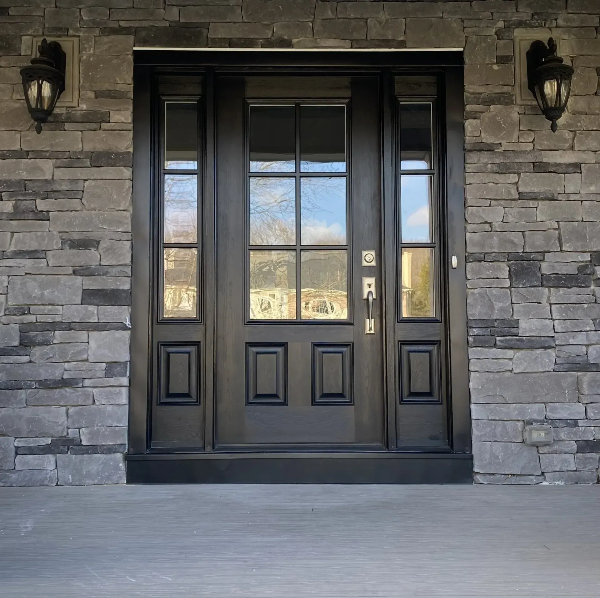 Black front door with glass panels set in a stone wall, flanked by two lanterns