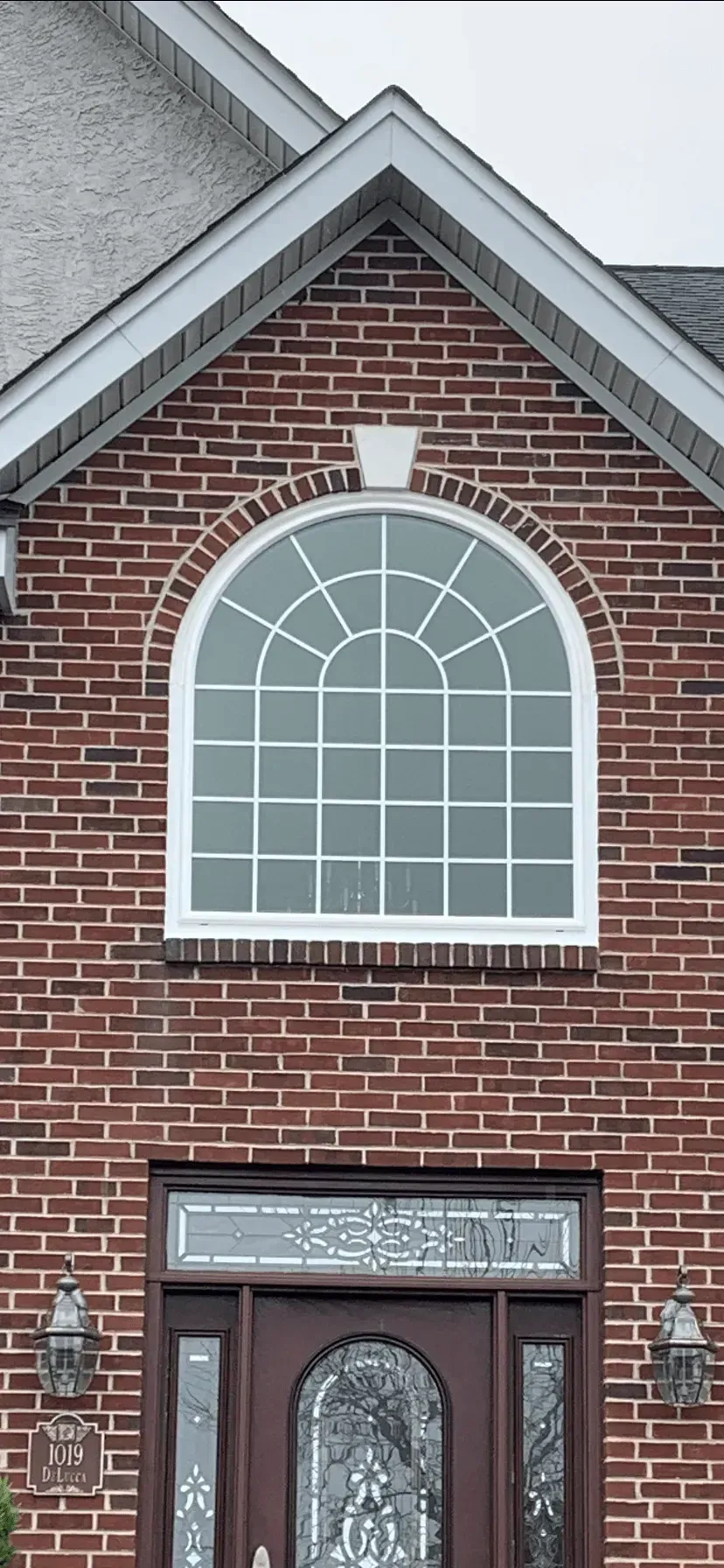Brick house facade with white-trimmed arched window above a red front door