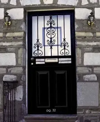 Black front door with ornate ironwork and wall-mounted lamps on a stone building. Black front door with ornate ironwork and wall-mounted lamps on a stone building.