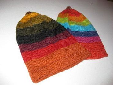 Two knit beanies with rainbow stripes. One is darker, the other brighter with a button on top.