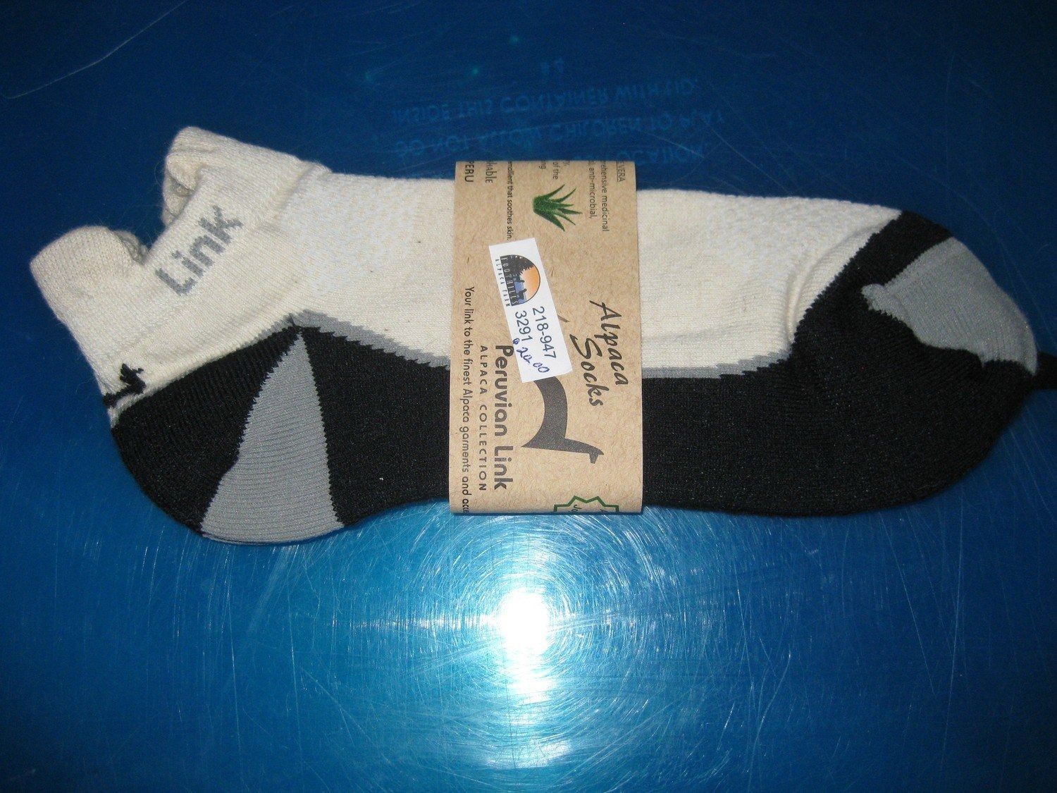 Pair of ankle socks with a beige upper, black heel and toe, and a gray accent, packaged with a brown paper band.