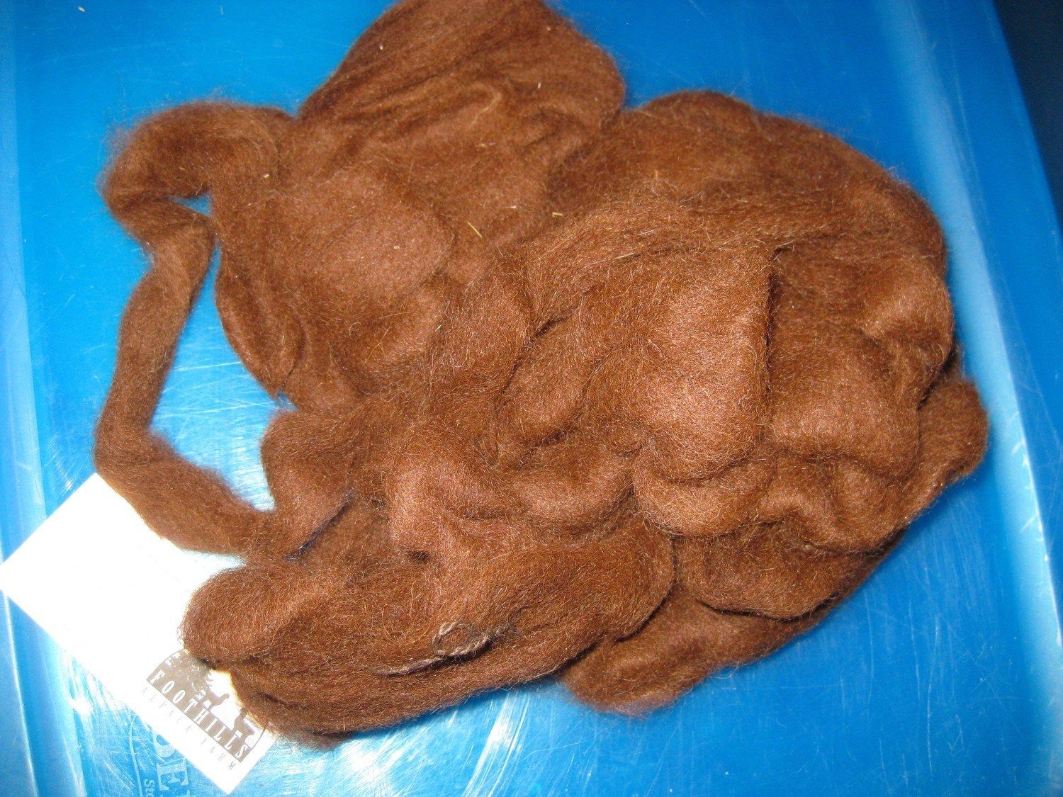 Brown wool fibers in a tangled mass on a blue surface. A white label with markings is on the left.