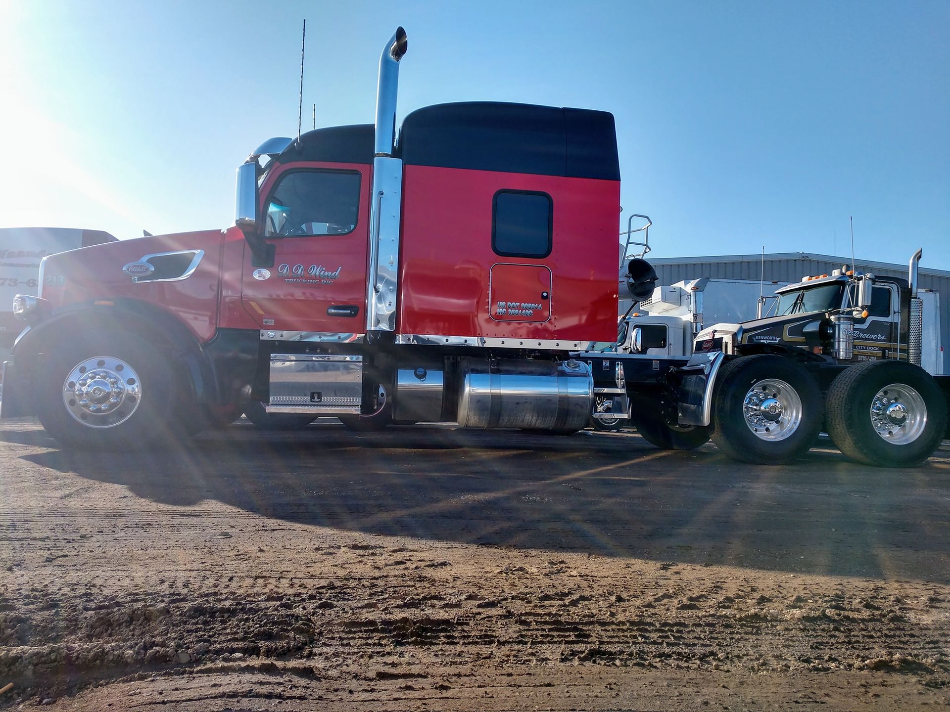 Red semi-truck parked on a dirt lot in bright sunlight.