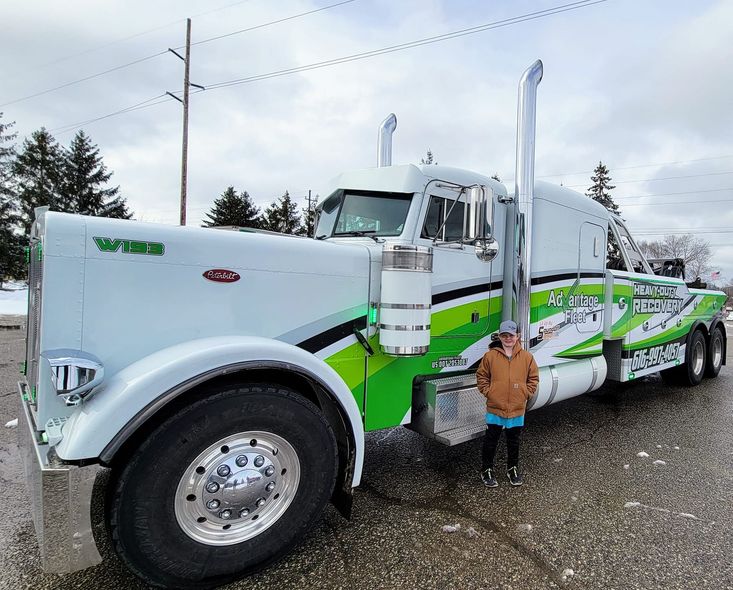 White and green semi truck parked outdoors, with a person standing beside the front wheel.