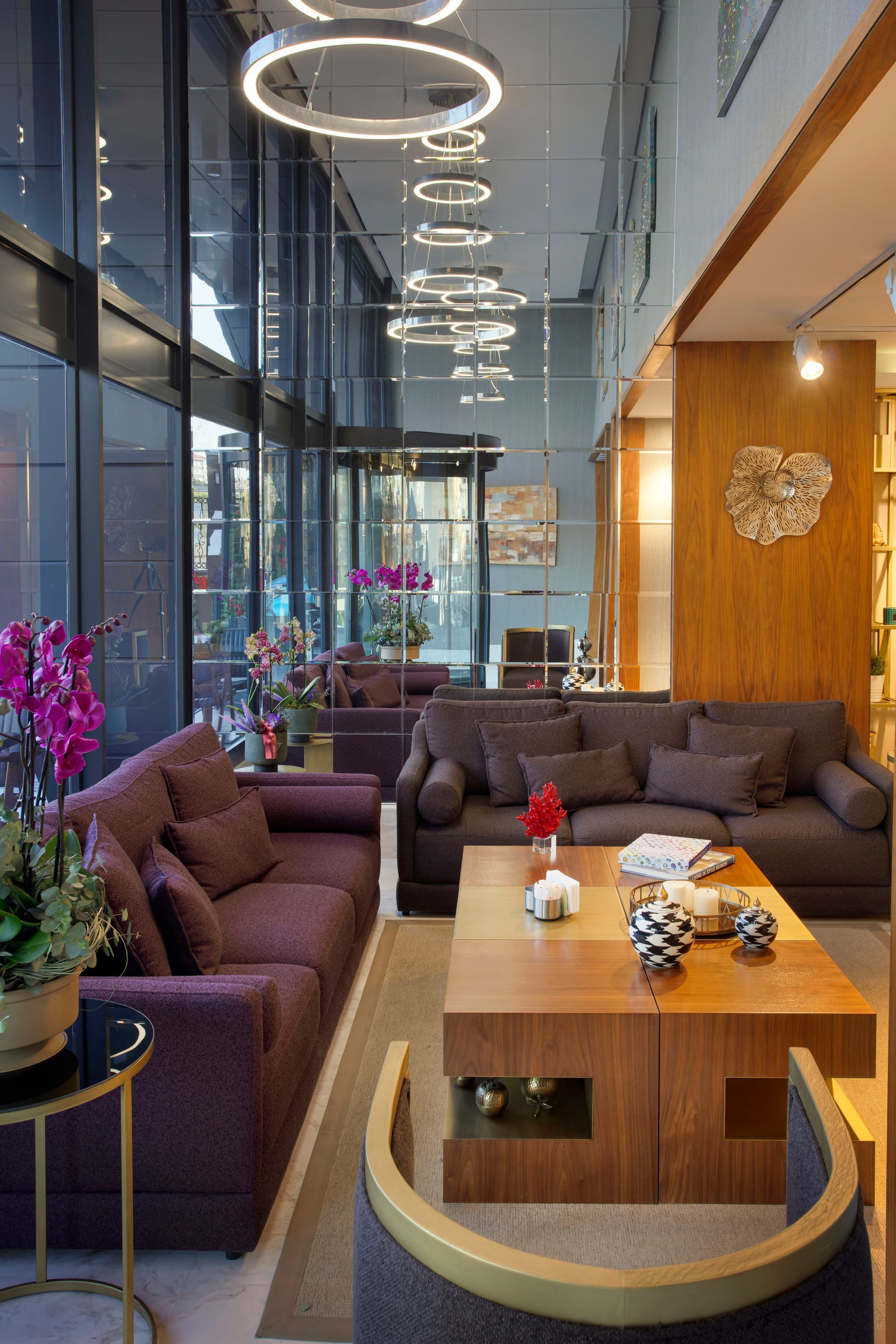 Mor kanepeler, ahşap masalar, asılı halka lambalar ve yerden tavana pencerelerle döşenmiş modern bir salon.
