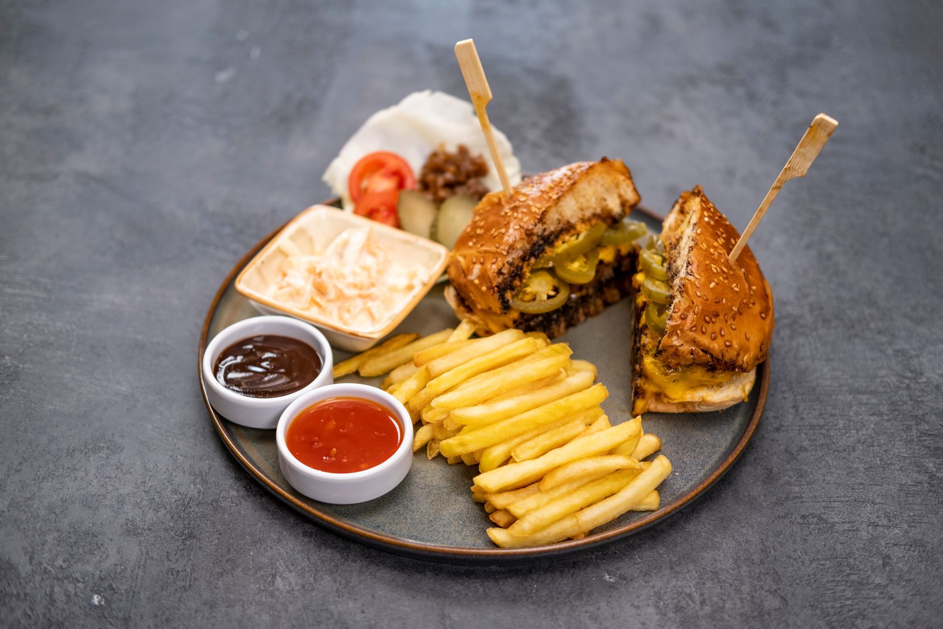 Koyu renkli bir tabakta, yanında patates kızartması, lahana salatası ve soslarla birlikte mini hamburger köfteleri.