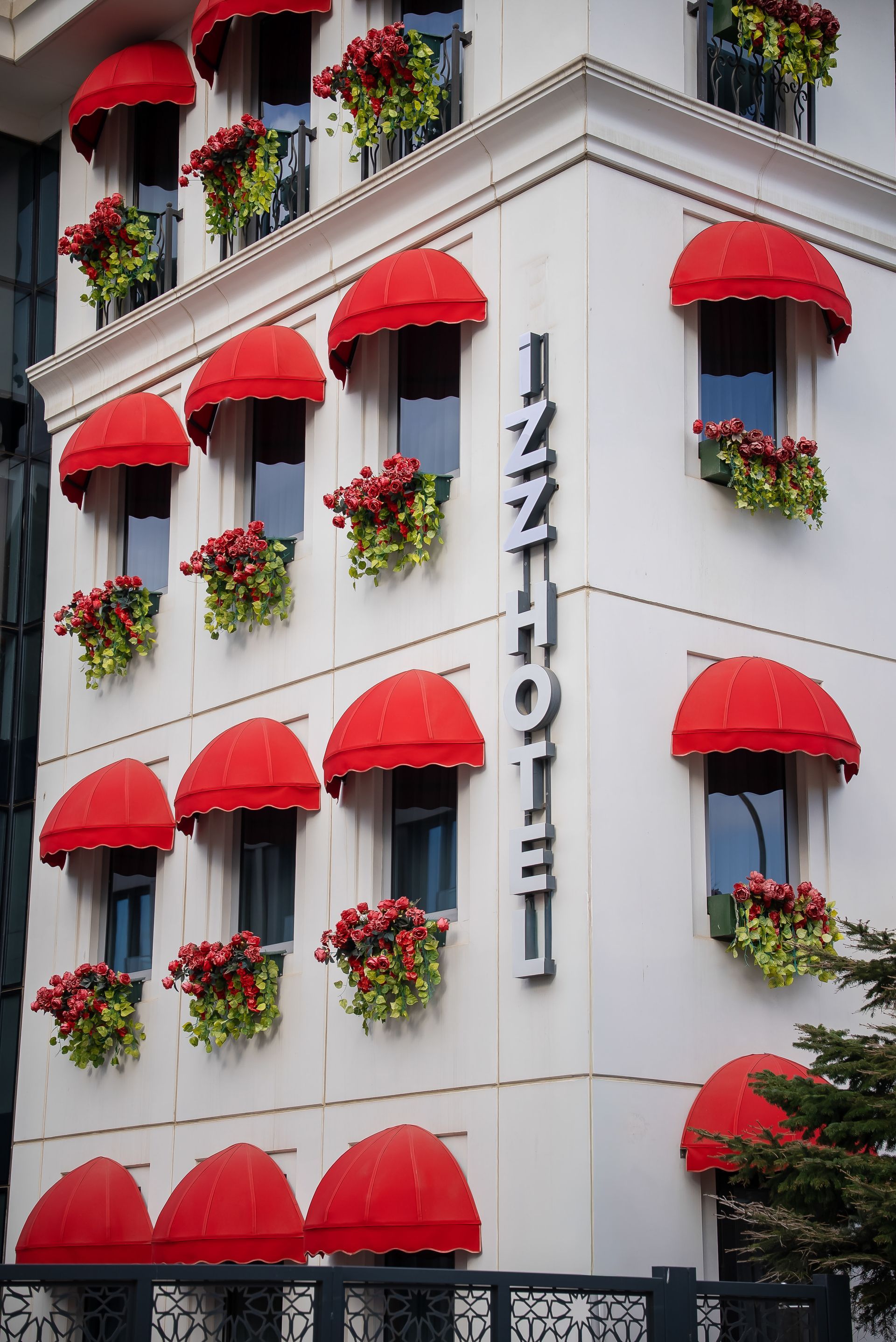 Kırmızı tenteler ve çiçek kutularıyla süslenmiş beyaz otel cephesi, üzerinde 