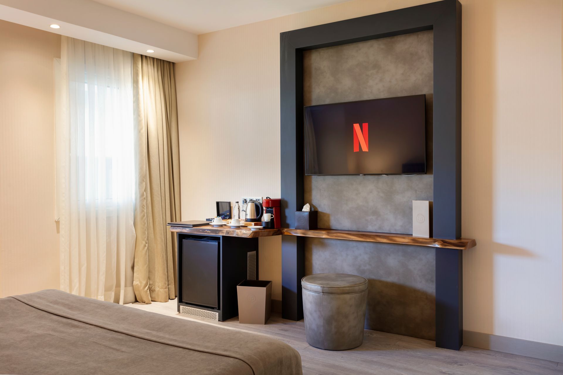 Modern otel odasında yatak, çalışma masası, sandalye ve duvara monte edilmiş televizyon bulunmaktadır.