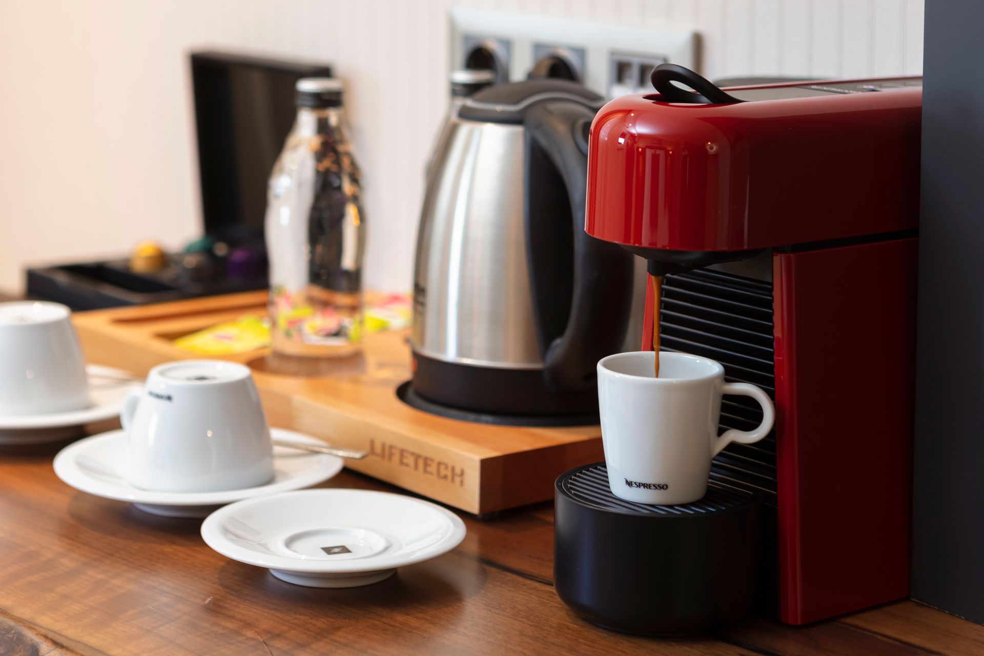 Ahşap tezgah üzerinde kırmızı bir espresso makinesi, su ısıtıcısı, fincanlar ve tabaklardan oluşan kahve köşesi.