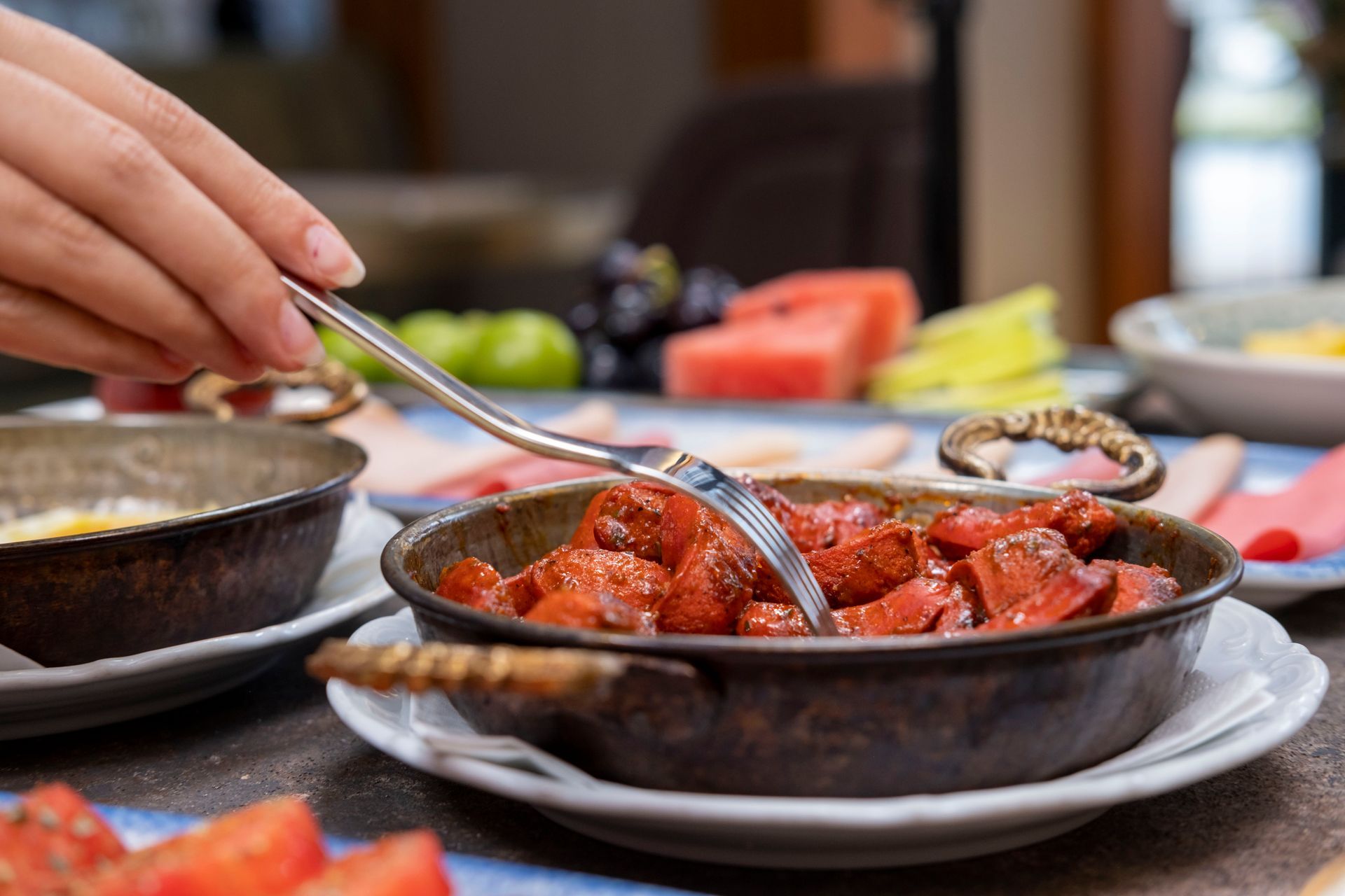Yemek masasında, diğer yemeklerin yanında, kırmızı soslu bir yemeği elle karıştıran bir kişi.