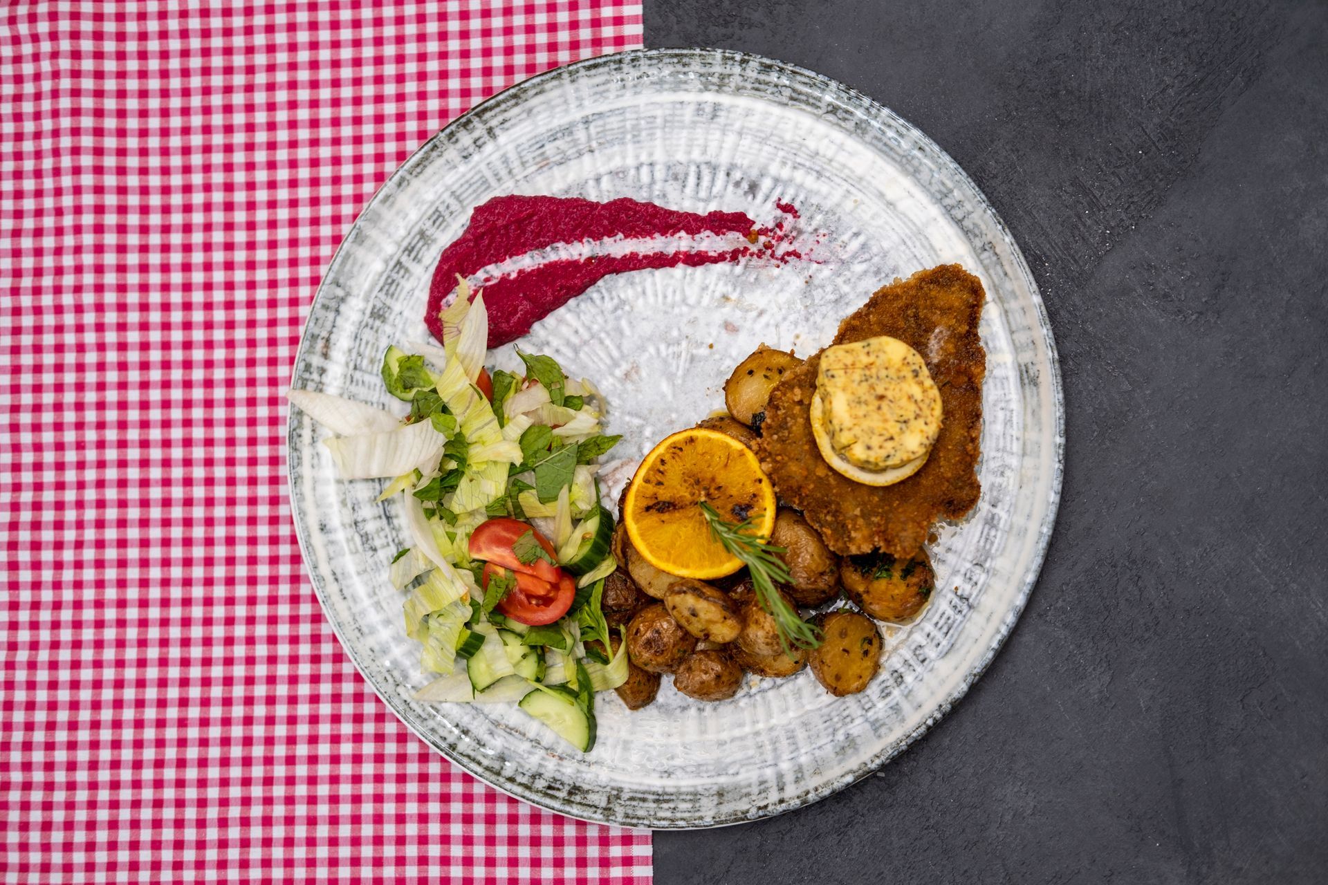 Kırmızı kareli masa örtüsü üzerinde beyaz bir tabakta limon ve salata eşliğinde ızgara et.