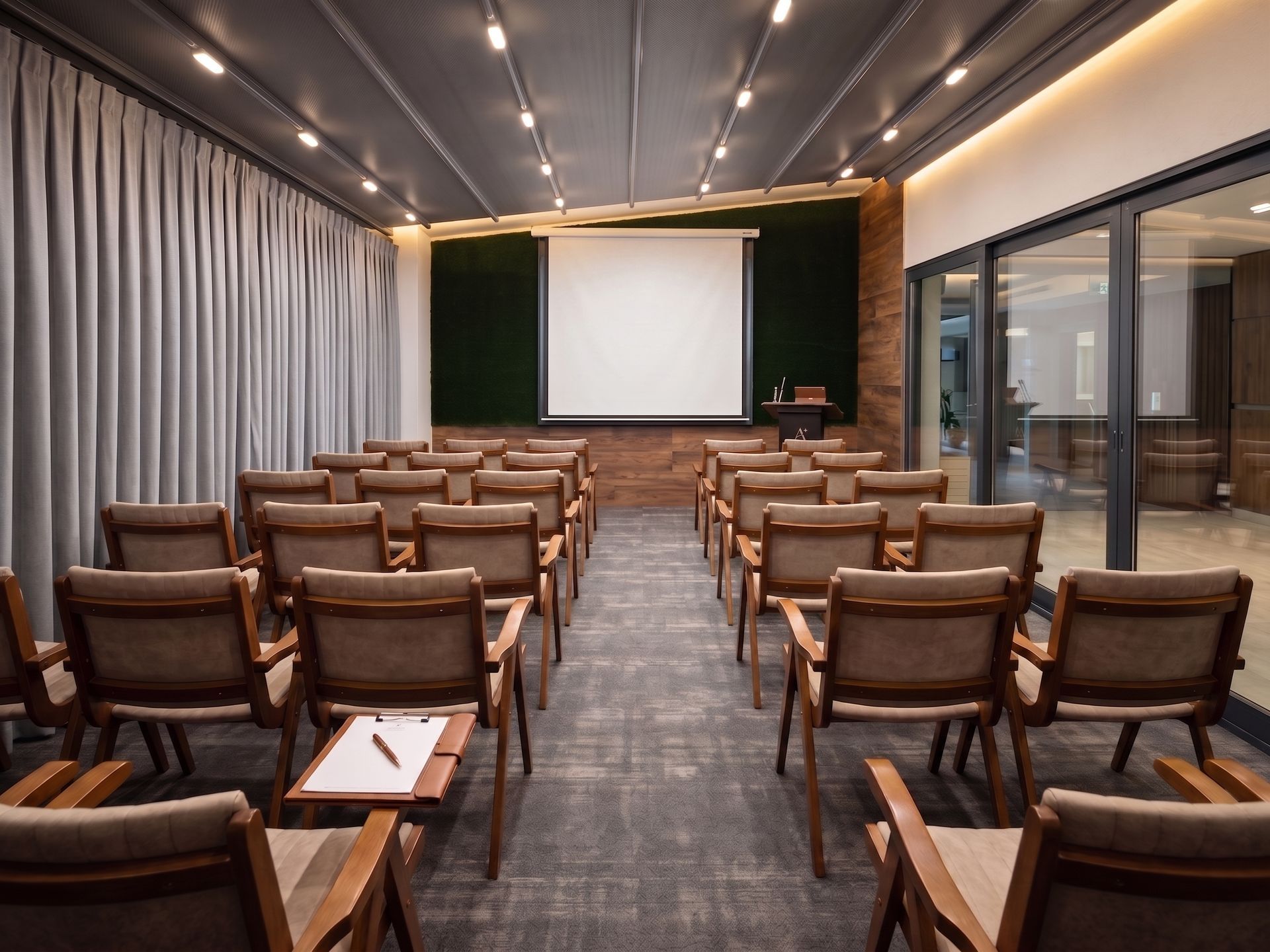 Conference room with rows of wooden chairs facing a projector screen and dark green presentation wall.